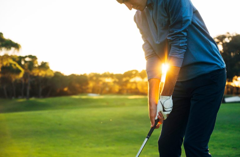 Male golf player teeing off golf ball from tee box to beautiful sunset